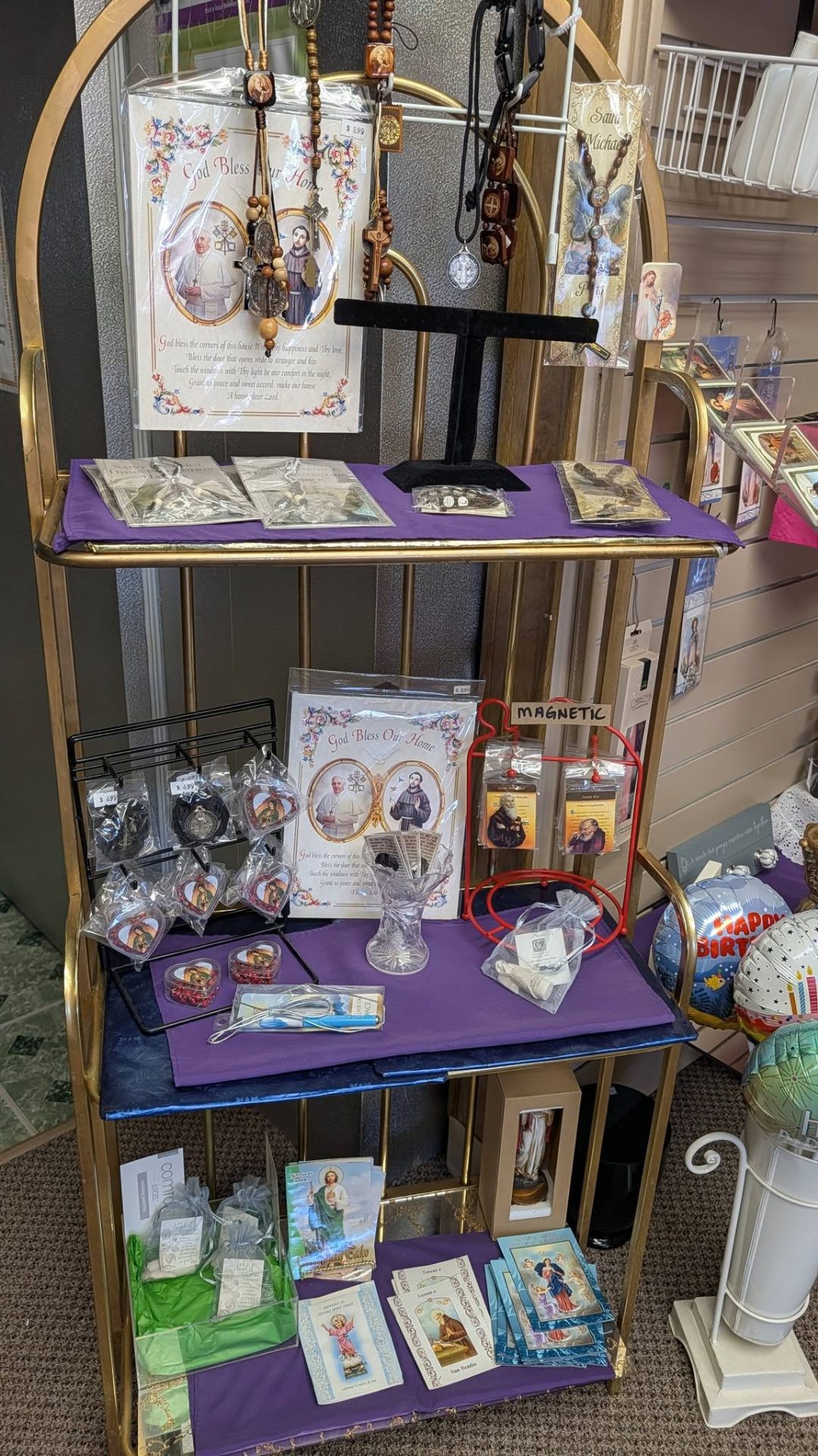 Brass rack of rosaries, prayer cards, and God Bless Our Home prints.