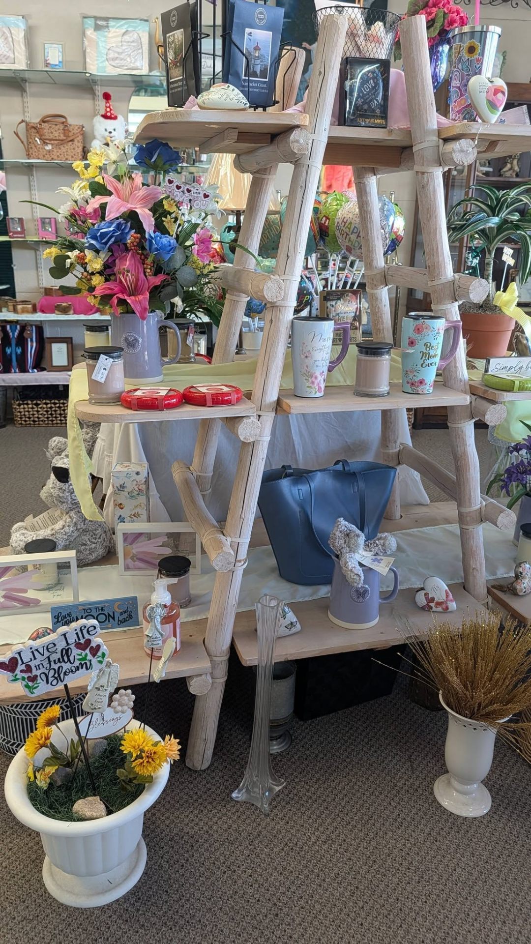 Tiered ladder display of mugs, candles, and floral pieces in the shop.